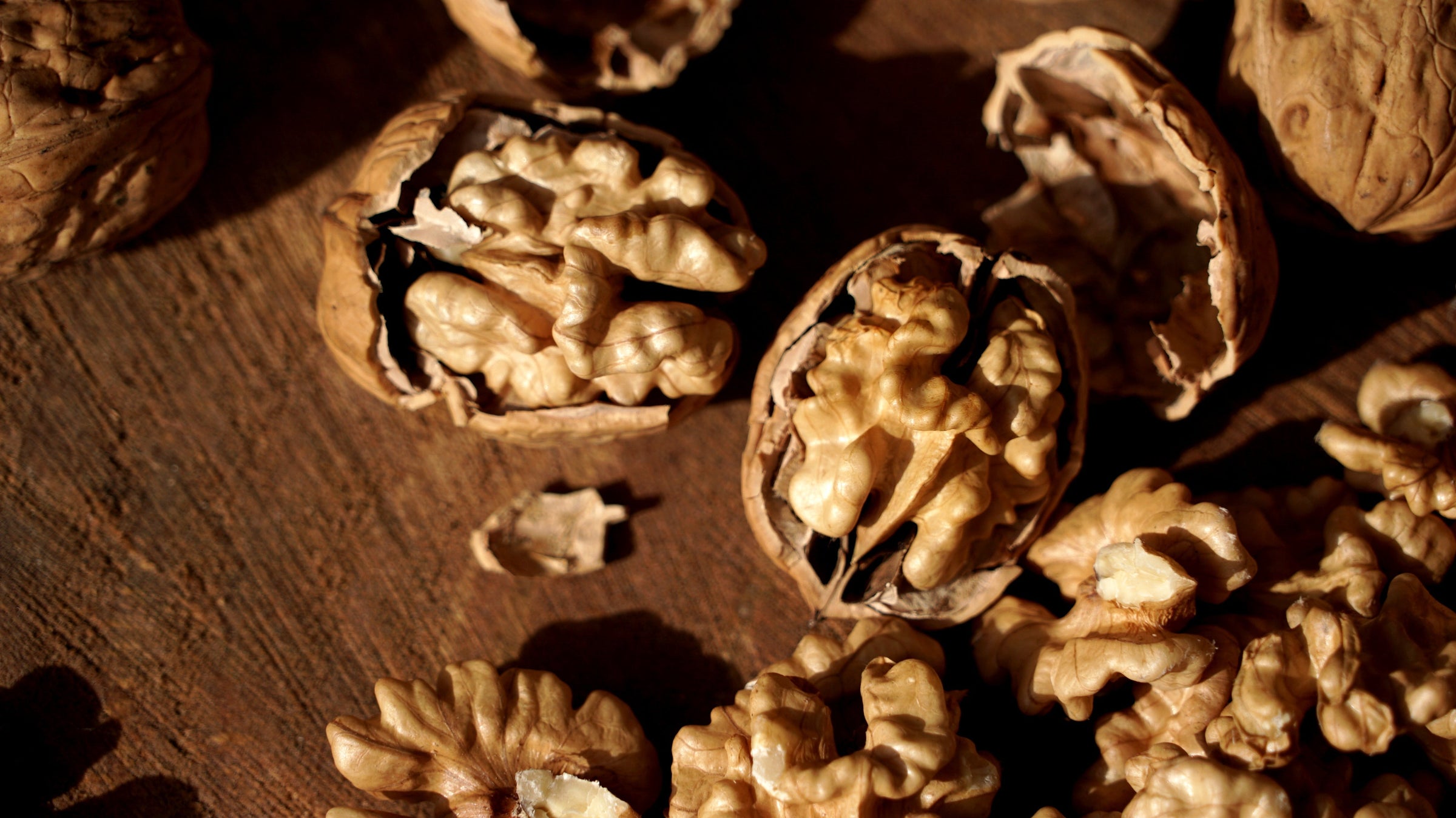 Cinco nueces sin cáscara ordenadas por distintos tonos de color, desde extra claro hasta ámbar oscuro, sobre una superficie de piedra con hojas verdes.